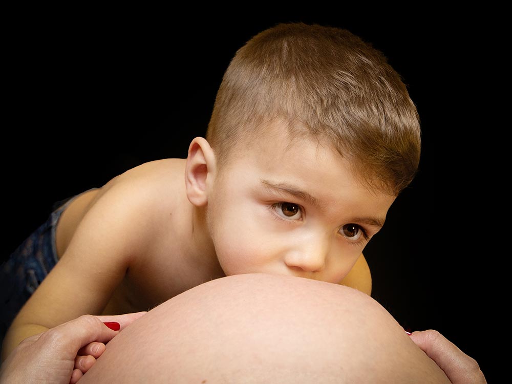 A Través De Un Objetivo niño besando panza a su madre